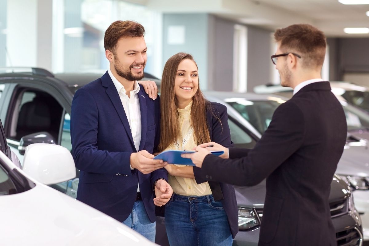 homem e mulher sorrindo enquanto recebem as chaves de um carro alugado.